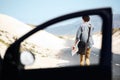 Exploring the countryside. Rear-view of a young man walking down the road holding a map, framed by a car door window in Royalty Free Stock Photo