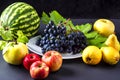 Exposition of fresh natural fruits, healthy food with many vitamin, watermelon, apple, grapes, pears on black background.