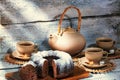 Exposition of hand made clay set on white wooden table and, with tasty chocolate cake. Tea cup and clay kettle.