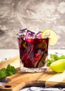 Exposition of red cocktail with ice cube and lime o wooden background, fresh drink.