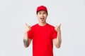 Express delivery, shipping and logistics concept. Upbeat handsome asian courier in red t-shirt and cap, show thumbs-up Royalty Free Stock Photo