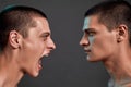 Expressing rage. Close up of two young angry caucasian twin brothers arguing, shouting while standing face to face