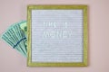 Expression - Time is money - written from white letters on letter board next to hundred-dollar bills on pink background. Royalty Free Stock Photo