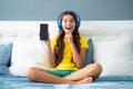 Expressive emotional excited teen girl. Teenager girl in headphones relax on bed at home using phone. Child in earphones