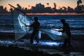 Expressive silhouette of fisherman catching fish fry, in the dark hours before dawn, among the waves on the beach.