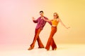 Expressive, talented, emotional couple, man and woman in stylish clothes dancing disco dance against gradient pink