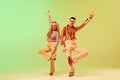 Expressive, talented young couple, man and woman in stylish vintage costumes dancing against gradient green yellow