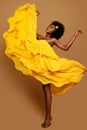 Expressive Woman dancing in Yellow Flying Dress. Happy Dark Skinned Dancer in Waving Fabric Gown. Model with Black curly Afro Hair Royalty Free Stock Photo