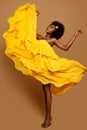 Expressive Woman dancing in Yellow Flying Dress. Happy Dark Skinned Dancer in Waving Fabric Gown. Model with Black curly Afro Hair