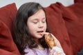 expressive young girl is eating chicken and vegetables for dinner on the couch while watching cartoons Royalty Free Stock Photo