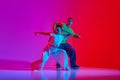 Expressive young man and woman in sportive clothes dancing hip hop, performing against pink red background in neon light Royalty Free Stock Photo