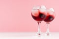 Exquisite arctic red alcoholic liquors with ice cubes, blueberry in two wineglasses on white wood table and pastel pink wall.