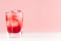 Exquisite cold red alcoholic liquor with ice cubes in shot glass closeup on white wood table and pastel pink wall, copy space.
