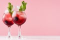 Exquisite red alcoholic shots of sweet berry liquor with ice cubes, blueberry, green mint on pastel soft light pink background. Royalty Free Stock Photo