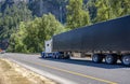 Extended cab white classic big rig semi truck tractor transporting cargo in tented black dry van semi trailer driving on the one Royalty Free Stock Photo