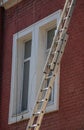 An extension ladder leans against the front of a multifamily housing building in preparation of roof repairs Royalty Free Stock Photo