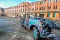 An exterior of an antique vintage roofless, roadster patterned car parked in front of an old school building in Berlin, Germany.