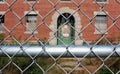 Exterior of boarded up and abandoned brick asylum hospital building with broken windows surrounded by chain link fence Royalty Free Stock Photo