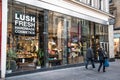 Exterior entrance to Lush handmade cosmetics store showing logo and branding. Shop window and pedestrian people walking past