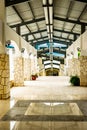 Exterior hallway corridor with high ceiling, lights and fixtures above and along stone wall columns