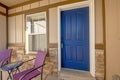 Exterior of a house with blue front door and purple armchairs and table