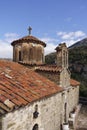 Greek Orthodox Monastery with cross above dome, against blue sky with clouds.