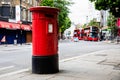 Exterior Red Royal Mail Pillar Post Box on street. Red bunk buses in the background Royalty Free Stock Photo