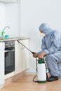 Exterminator Spraying Pesticide On Wooden Cabinet