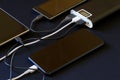 An external battery - a powerbank with three gadgets connected to it lies on a dark background. The concept of recharging a Royalty Free Stock Photo