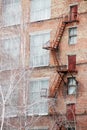 External fire escape staircase on an old brick building of factory, plant. Big windows, white birch trees grows near. Royalty Free Stock Photo