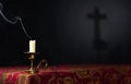 Extinguished candle on a dark background with the silhouette of a cross, selective focus