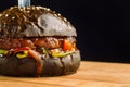 Close-up of delicious fresh home made beef burger with lettuce, cheese, onion and tomato. Black bun. Royalty Free Stock Photo