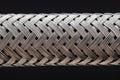 Extra Close-up of a metal hose, with crisscrossed silver strands, isolated on black background. Macro shot.