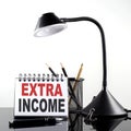 EXTRA INCOME text on notebook with pen and table lamp on the black background