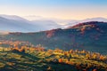 Extraordinary autumn landscape. Green fields with haystacks. Trees covered with orange and crimson leaves. Mountain landscapes.