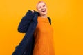 Extraordinary beautiful woman with short pink hair in dark coat smiles isolated on orange background