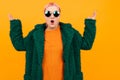 Extraordinary beautiful woman with short pink hair in dark coat and sunglasses is shocked isolated on orange background