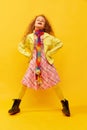 Extraordinary look. Little cute girl, child with curly hair posing in bright clothes over yellow studio background