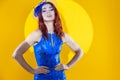 Extravagant Caucasian Ginger Woman in Blue Artistic Dance Suit Posing In Shawl Hat With Circular Shaped Light On Yellow Background