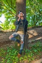 Extravagant hipster male model listen to music in nature. The model wears a leather jacket with rivet and a white scarf Royalty Free Stock Photo