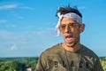 Extravagant hipster male model with sunglasses and a white scarf on a wooden bridge. The model showing a tongue. Royalty Free Stock Photo