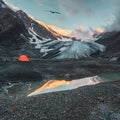 Extreme camping. Orange reinforced tent against the background of a big glacier on a high-altitude plateau. Mountaineering camp at