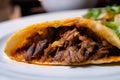 Extreme close-up of a beef taco on a plate, showing the juicy and tender meat filling, the crispy and slightly charred shell