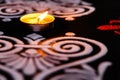 Extreme close up of glowing tea lamp and white red rangoli art on black background. diwali concept