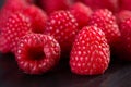 Extreme close up of a group of fresh, ripe, organic raspberries on a black board. Selective focus. Macro texture food background Royalty Free Stock Photo