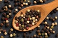 Extreme close up of a mix of black, red, green and white peppercorns in a wooden spoon on a black, rustic stone kitchen board. Royalty Free Stock Photo