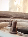 Extreme close up of old rustic bolt nut fastener on the wheel rim of a tire - vehicle part. Rusty rust colored iron metal.