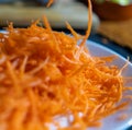 Pile of grated carrot on white plate with blurry background