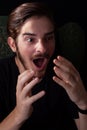 Extreme close up of young adult male mouth open, both hands up in shock or surprise. Deep color tones for dramatic effect, dark