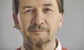 Closeup portrait of serious senior man looking at camera on grey studio background